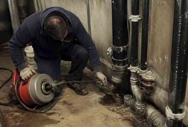 Instalatér v suterénu čistí odpadní potrubí strojem s rotující pružinou