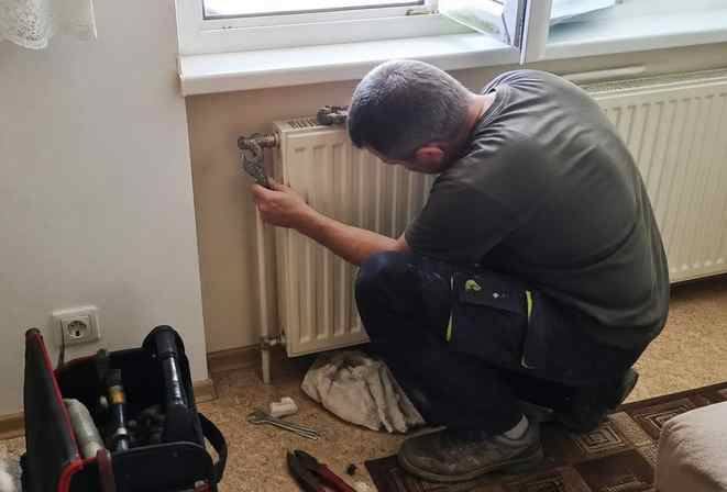 Technik v bytě opravuje ventil na radiátoru pod oknem